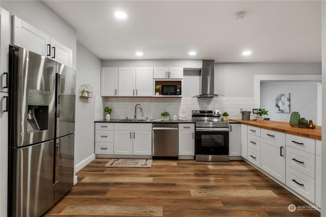 kitchen featuring wall chimney exhaust hood, white cabinetry, stainless steel appliances, and wooden counters