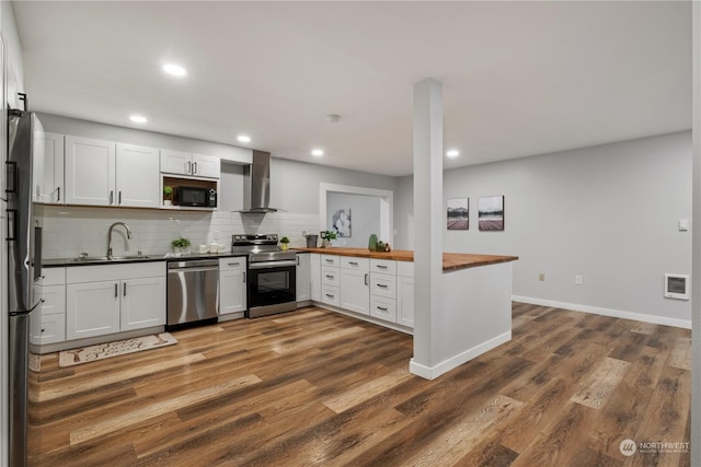 kitchen with wall chimney range hood, sink, butcher block countertops, white cabinetry, and stainless steel appliances