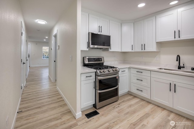 kitchen with light hardwood / wood-style floors, white cabinetry, sink, and appliances with stainless steel finishes