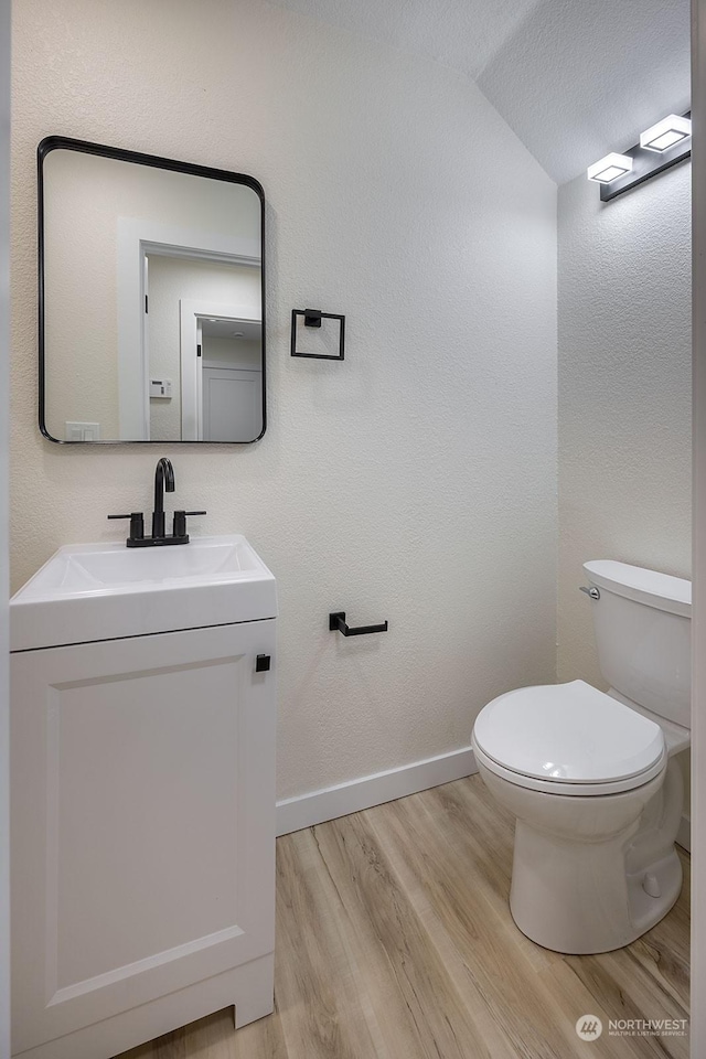 bathroom with hardwood / wood-style floors, vanity, toilet, and vaulted ceiling