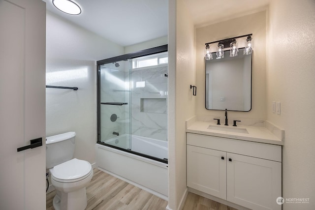 full bathroom featuring hardwood / wood-style flooring, vanity, toilet, and bath / shower combo with glass door