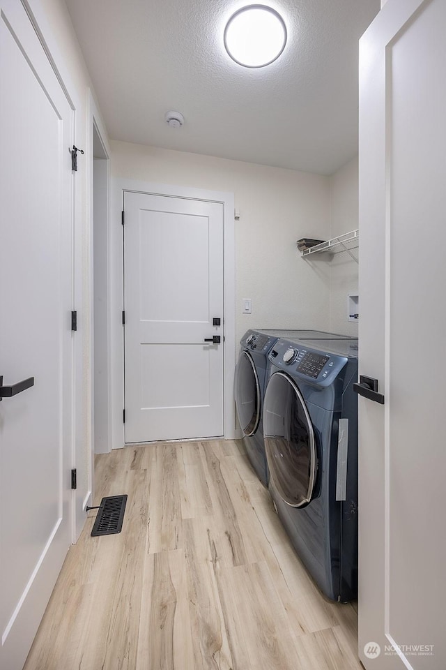 clothes washing area with washer and dryer, a textured ceiling, and light hardwood / wood-style flooring