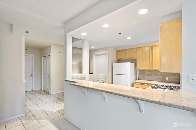 kitchen featuring a breakfast bar, light brown cabinets, white appliances, backsplash, and kitchen peninsula