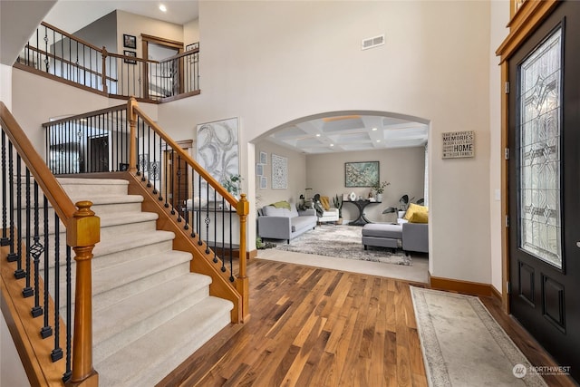 foyer entrance with beamed ceiling, wood-type flooring, a high ceiling, and coffered ceiling