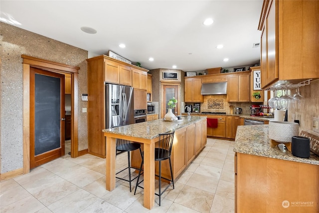 kitchen with decorative backsplash, light stone countertops, range hood, a kitchen island, and a kitchen bar