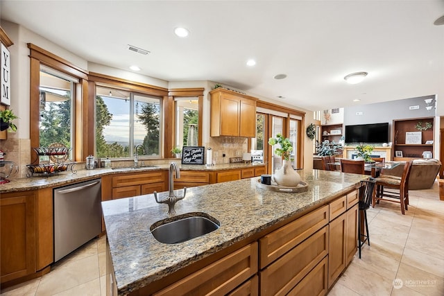 kitchen featuring light stone counters, sink, an island with sink, and stainless steel dishwasher