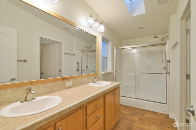 bathroom with vanity, lofted ceiling with skylight, backsplash, walk in shower, and wood-type flooring