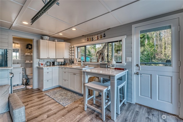 kitchen with sink, white cabinets, light hardwood / wood-style flooring, and wooden walls