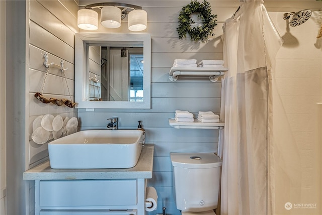 bathroom featuring wood walls, toilet, and vanity