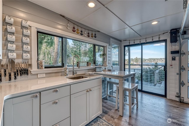 kitchen featuring sink, light wood-type flooring, light stone counters, and white cabinets