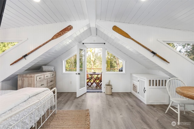 bedroom featuring wood walls, light wood-type flooring, and lofted ceiling with beams