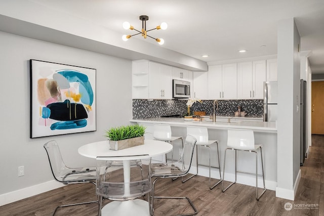 kitchen with kitchen peninsula, stainless steel appliances, an inviting chandelier, white cabinetry, and a kitchen breakfast bar