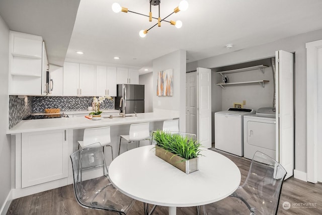 kitchen featuring wood-type flooring, washer and clothes dryer, kitchen peninsula, stainless steel fridge, and white cabinetry