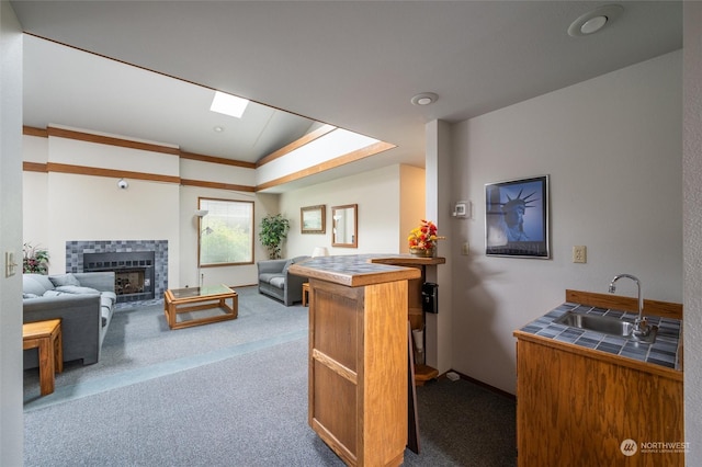 living room featuring a tiled fireplace, lofted ceiling with skylight, sink, and light colored carpet