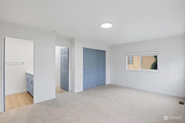 unfurnished bedroom with a closet, light carpet, and ensuite bath