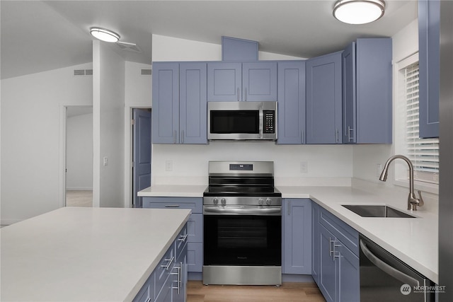 kitchen with lofted ceiling, sink, stainless steel appliances, blue cabinetry, and light wood-type flooring