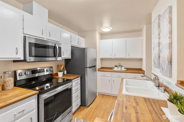 kitchen with white cabinetry, sink, stainless steel appliances, wood counters, and light hardwood / wood-style floors