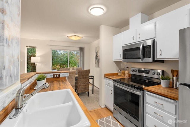 kitchen featuring stainless steel appliances, sink, white cabinets, light hardwood / wood-style floors, and butcher block counters