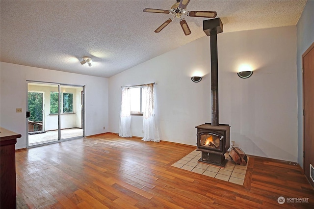 unfurnished living room with vaulted ceiling, hardwood / wood-style floors, a textured ceiling, and a wood stove