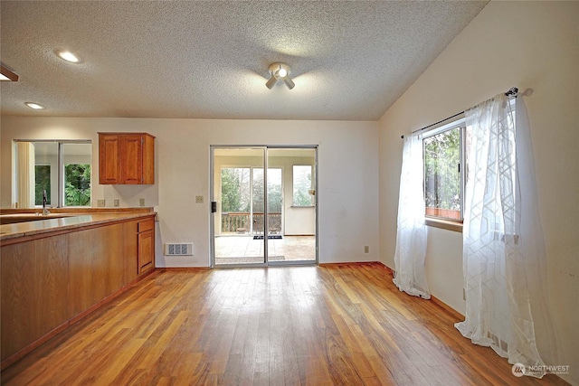 kitchen with a textured ceiling, a sink, visible vents, light wood-type flooring, and brown cabinets