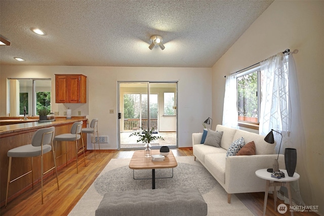 living area featuring visible vents, a textured ceiling, and light wood finished floors