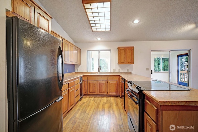 kitchen featuring a peninsula, a textured ceiling, light wood-type flooring, recessed lighting, and black appliances