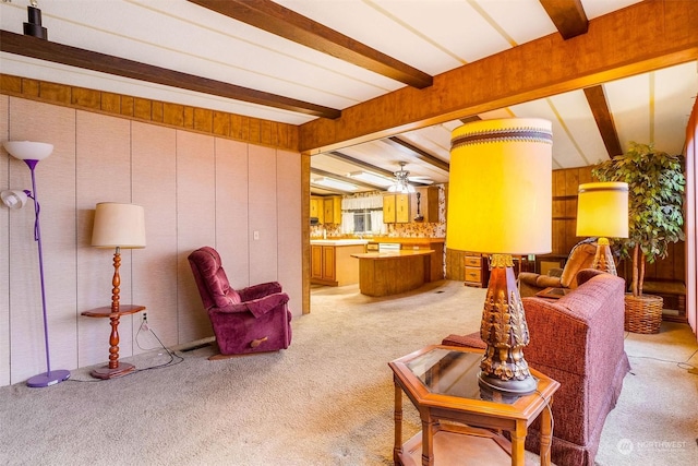 living room featuring beamed ceiling, ceiling fan, wood walls, and light carpet