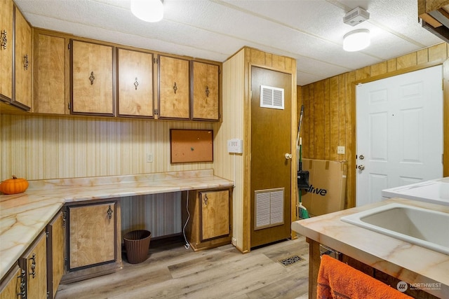 kitchen featuring wooden walls, sink, and light wood-type flooring