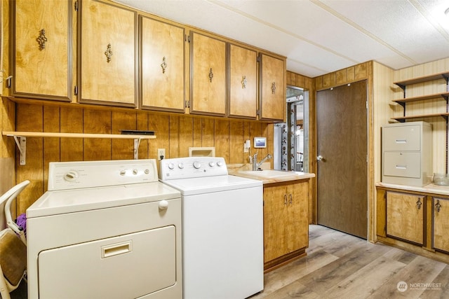 washroom featuring cabinets, wooden walls, sink, light hardwood / wood-style flooring, and washing machine and dryer