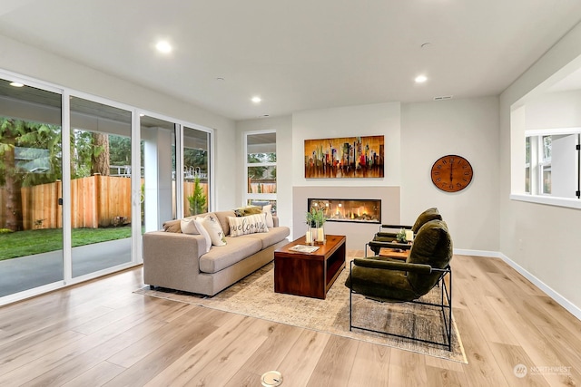 living room with plenty of natural light, light wood-type flooring, a glass covered fireplace, and baseboards