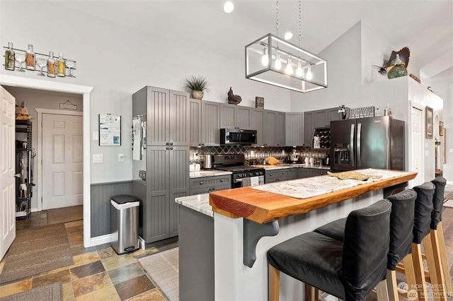 kitchen with decorative backsplash, gray cabinetry, stainless steel appliances, high vaulted ceiling, and a breakfast bar area