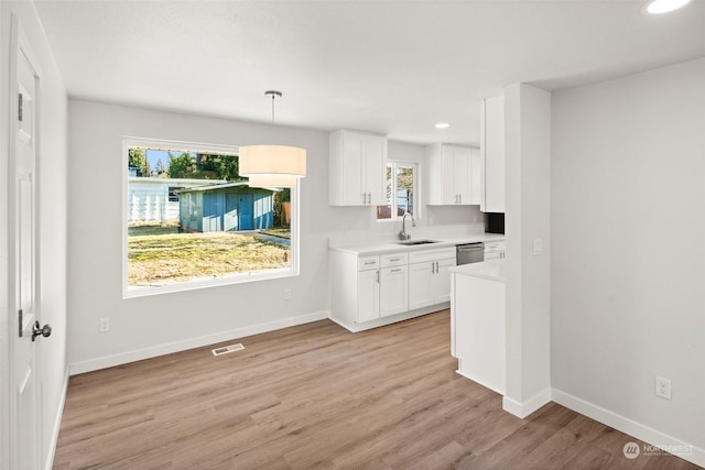 kitchen with sink, white cabinetry, hanging light fixtures, light hardwood / wood-style flooring, and stainless steel dishwasher