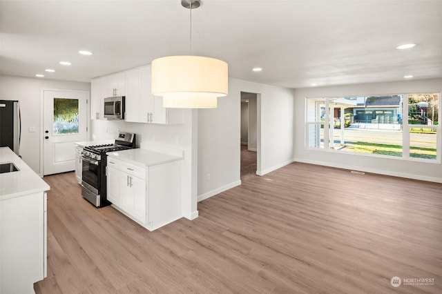 kitchen with stainless steel appliances, pendant lighting, white cabinets, and light wood-type flooring