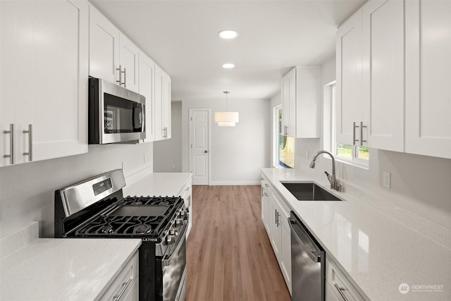 kitchen with sink, appliances with stainless steel finishes, white cabinetry, light hardwood / wood-style floors, and decorative light fixtures