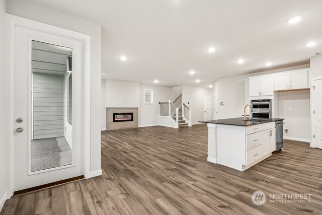 kitchen featuring an island with sink, dark hardwood / wood-style floors, white cabinets, and double oven