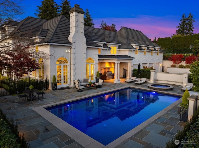 back house at dusk featuring a swimming pool with hot tub, a patio, and french doors