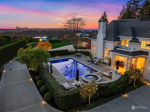 pool at dusk with an in ground hot tub and a patio area