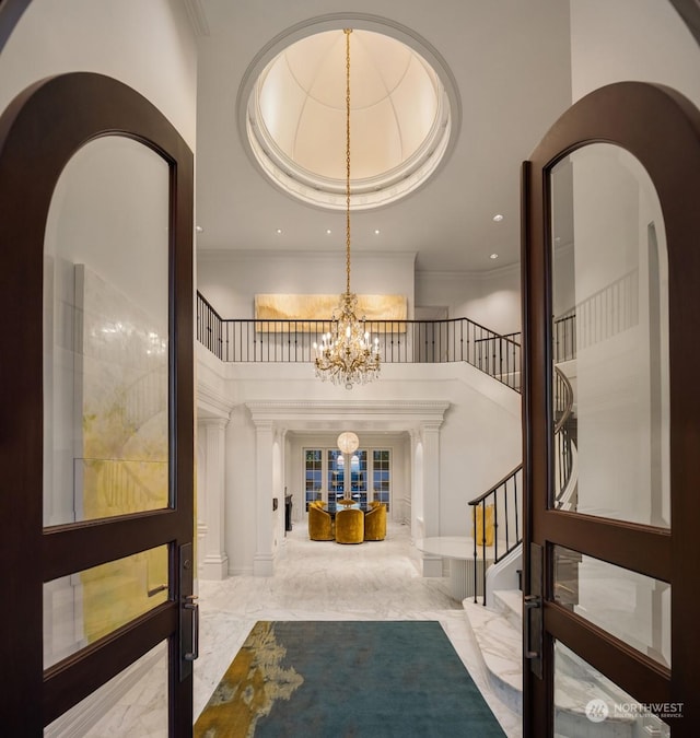 entryway featuring ornate columns, crown molding, a towering ceiling, and a notable chandelier