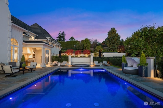 pool at dusk featuring an in ground hot tub and a patio