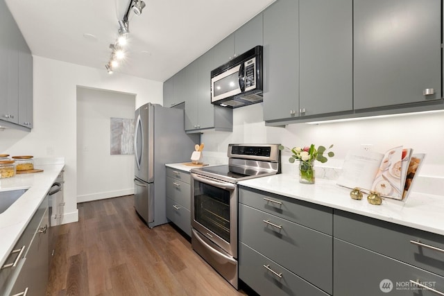 kitchen with hardwood / wood-style floors, gray cabinets, light stone countertops, and appliances with stainless steel finishes