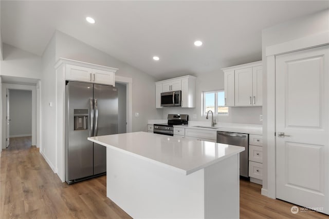 kitchen with a center island, sink, vaulted ceiling, appliances with stainless steel finishes, and white cabinetry