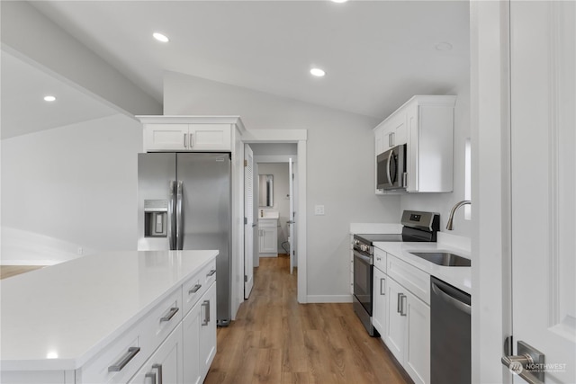 kitchen featuring lofted ceiling, sink, appliances with stainless steel finishes, light hardwood / wood-style floors, and white cabinetry