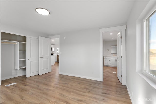 unfurnished bedroom with ensuite bath, a closet, and light wood-type flooring