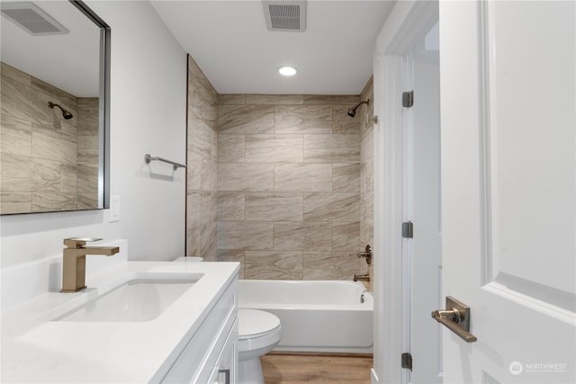 full bathroom with hardwood / wood-style floors, vanity, tiled shower / bath combo, and toilet