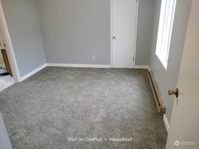 carpeted empty room featuring a baseboard heating unit