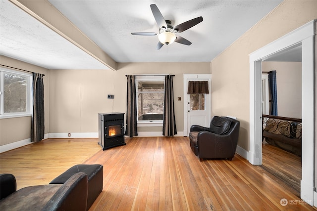 living room with a textured ceiling, hardwood / wood-style flooring, a wood stove, and ceiling fan