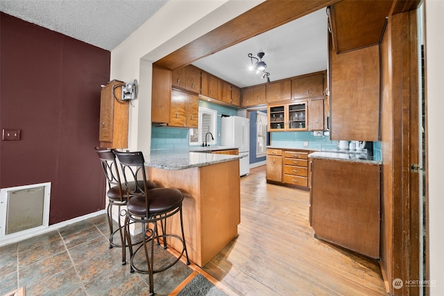 kitchen with kitchen peninsula, backsplash, a textured ceiling, white refrigerator, and a breakfast bar area