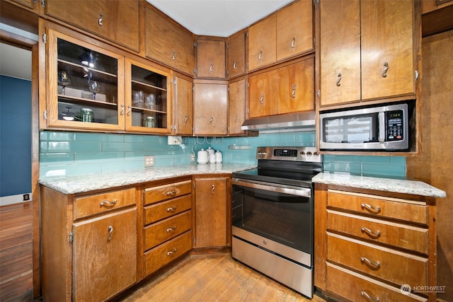 kitchen featuring appliances with stainless steel finishes, light wood-type flooring, extractor fan, and light stone counters