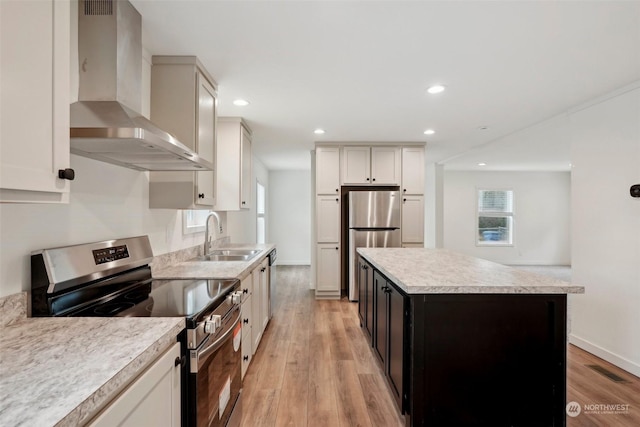 kitchen with stainless steel appliances, sink, wall chimney range hood, white cabinets, and a center island