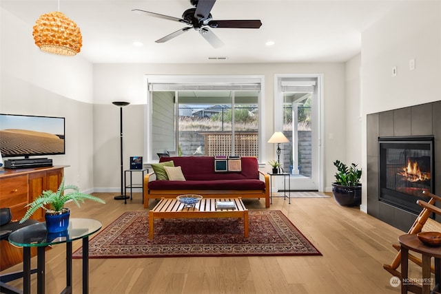 interior space featuring a tile fireplace, ceiling fan, and light wood-type flooring